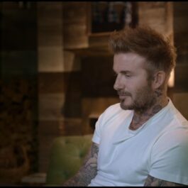David Beckham, într-un tricou alb, pe o canapea, cu capul plecat