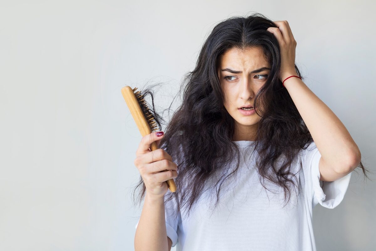 O femeie privește îngrozită o perie de păr plină de fire rupte în timp ce așază o palmă peste o latură a părului