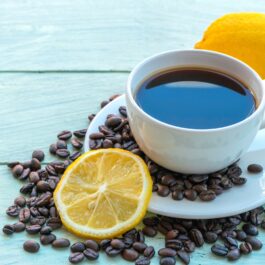 O ceașcă cu cafea cu lămâie pusă alături de o felie de lămâie pentru a ilustra modul în care cafeaua cu lămâie te-ar putea ajuta să slăbești
