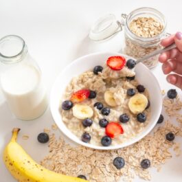 O masă pe care se află un pahar cu lapte, o banană și un bol cu terci de ovăz pentru a ilustra ce se întâmplă dacă mănânci fulgi de ovăz în fiecare dimineață