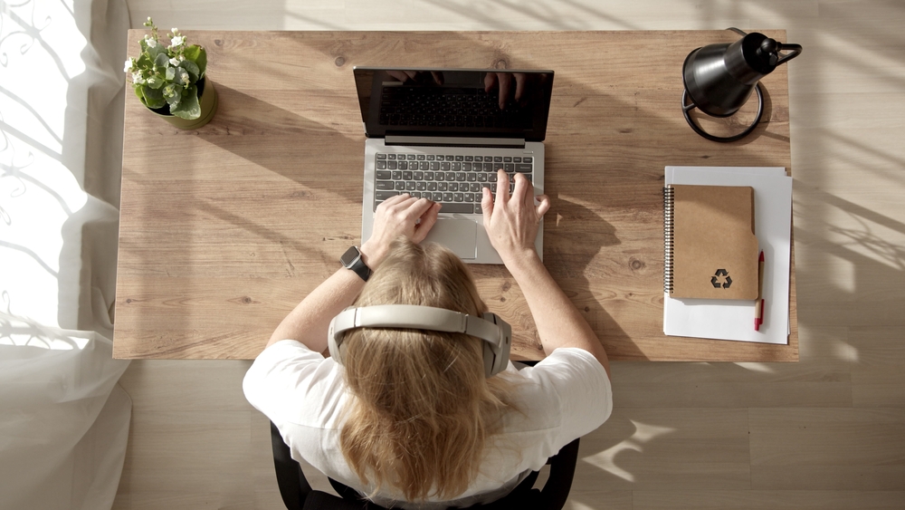 O femeie care stă pe scaun, la birou și lucrează la laptop