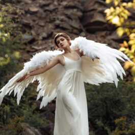 O femeie frumoasă, îmbrăcată într-o rochie albă cu aripi de înger în spate