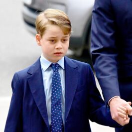 Prințul George, îmbrăcat la costum, în timp ce se plimbă de mână cu tatăl său