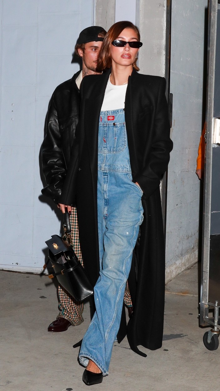 Hailey Bieber, într-o salopetă din denim, cu un palton negru peste