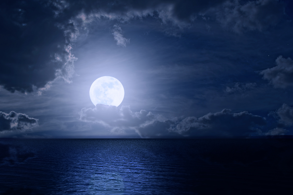 Lună Plină deasupra mării pe un fundal închis la culoare cu nori