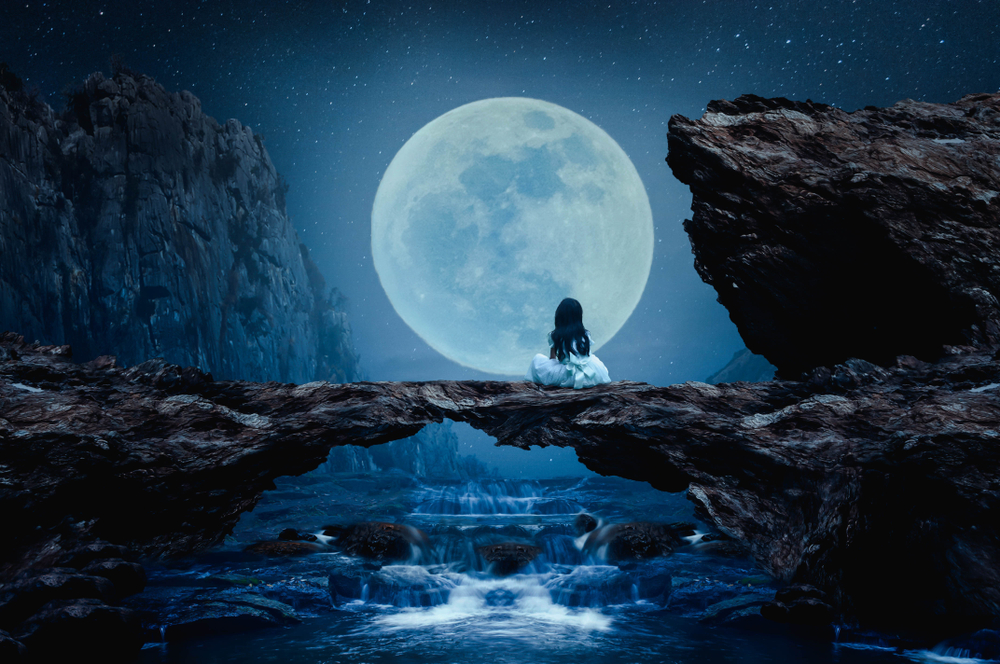 Fată îmbrăcată în alb stă cu fața îndreptată spre luna plină deasupra unui lac