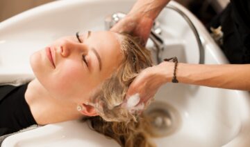 O femeie cu părul blond care se află la salon și este spălată pe păr cu metoda co-wash