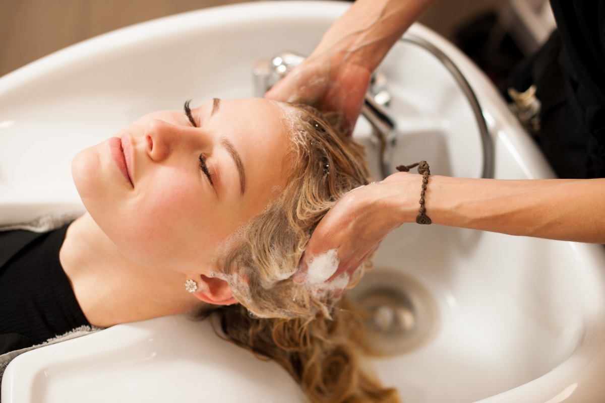 O femeie cu părul blond care se află la salon și este spălată pe păr cu metoda co-wash