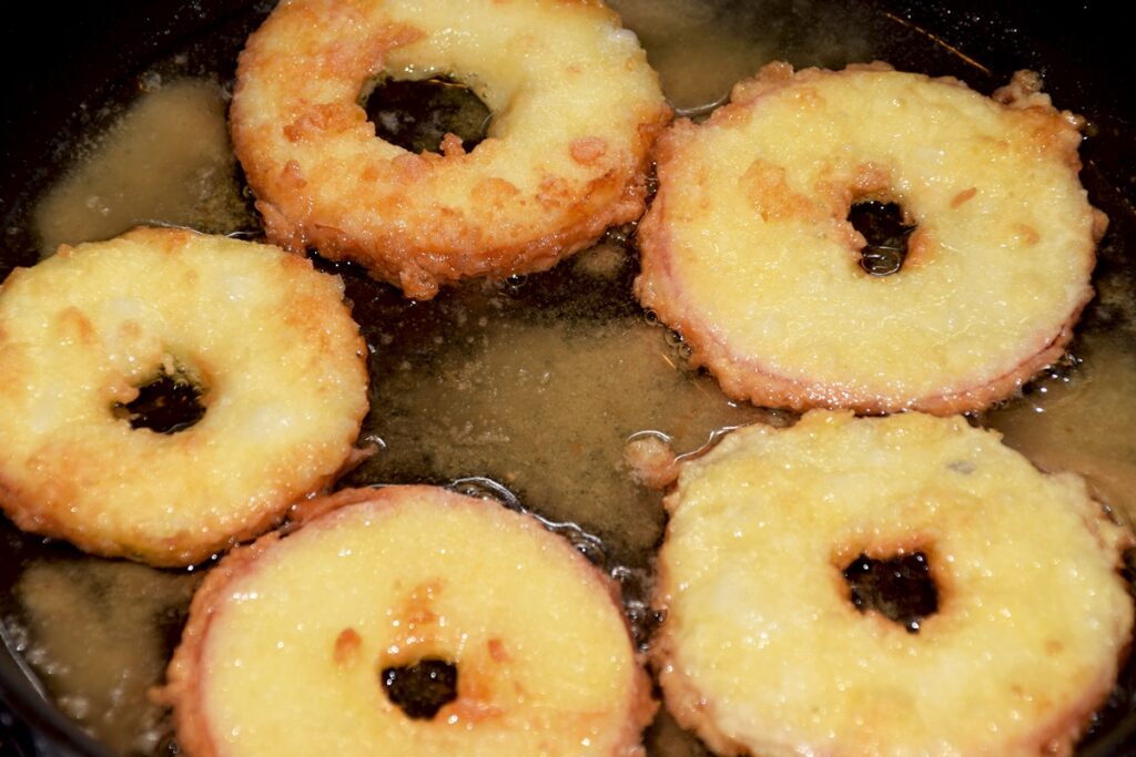 Cinci rondele de mere în aluat de clătite prăjite în tigaia cu ulei