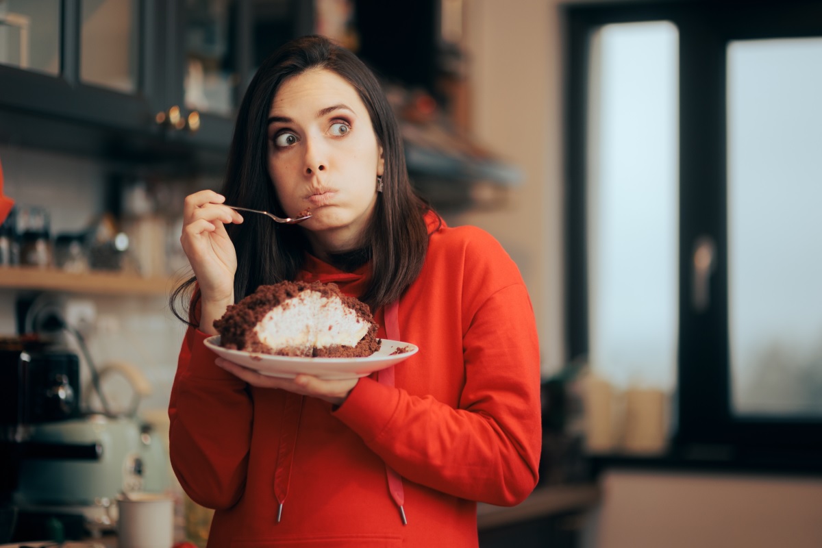 O femeie frumoasă care poartă un pulover roși și mănâncă dintr-o prăjitură cu ciocolată pentru a ilustra ce poți face pentru reducerea poftei de mâncare