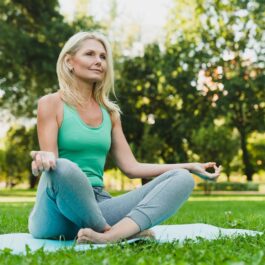 O femeie care are peste 50 de ani și stă în parc în timp ce practică yoga