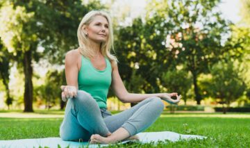 O femeie care are peste 50 de ani și stă în parc în timp ce practică yoga
