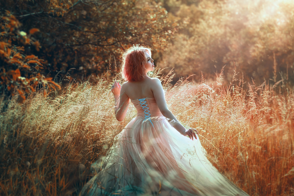 O femeie frumoasă, îmbrăcată într-o rochie de zână, într-un câmp de toamnă