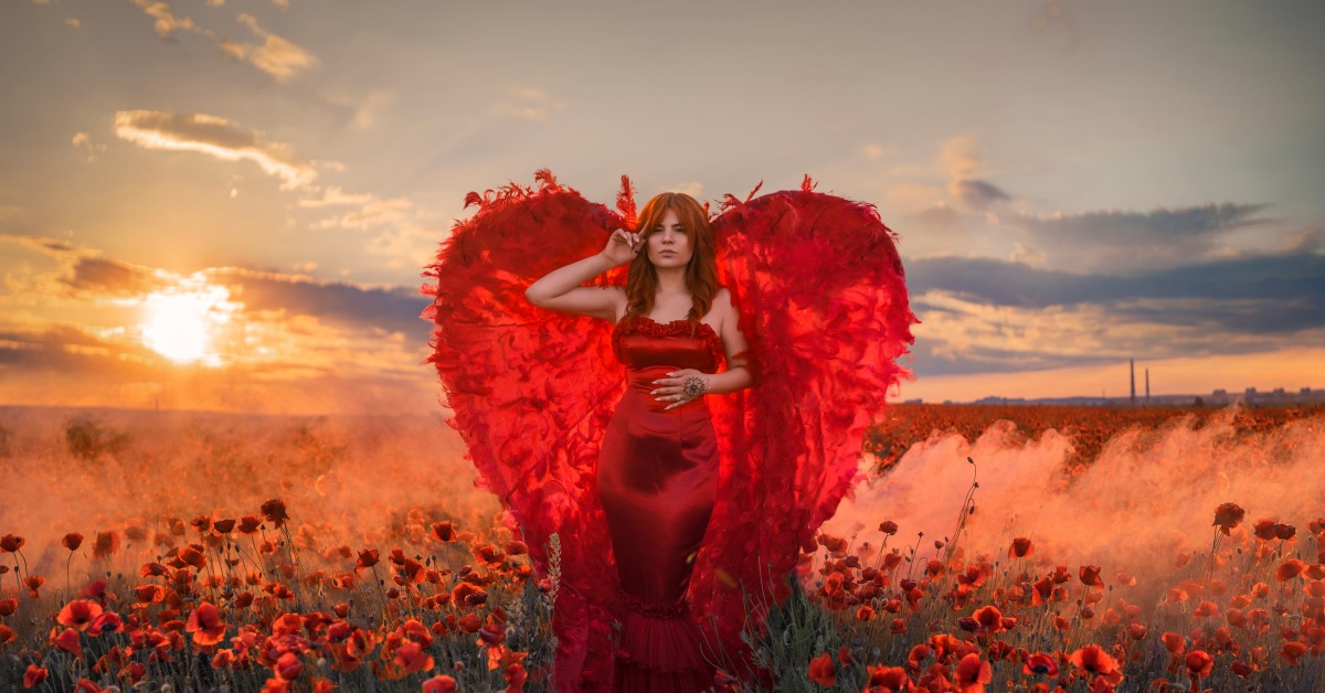 O femeie frumoasă care poartă o rochie roșie și aripi de înger pentru a ilustra una dintre cele 4 zodii de femei care seduc orice bărbat