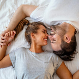 O femeie și un bărbat în pat, cu zâmbetul pe buze