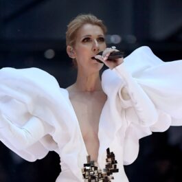 Celine Dion într-o rochie albă în timp ce cântă pe scenă la un microfon