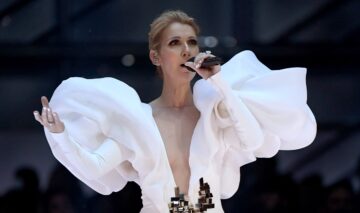 Celine Dion într-o rochie albă în timp ce cântă pe scenă la un microfon
