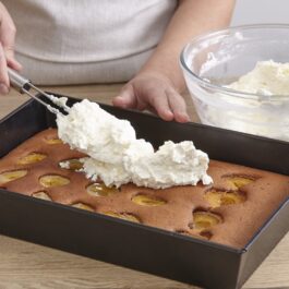 Femeie adăugând crema peste blatul prăjiturii