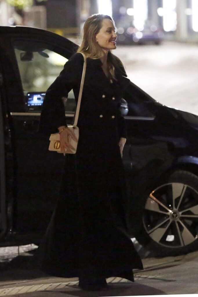 Angelina Jolie într-un palton negru și cu o poșetă pe umăr în timp ce iese din mașină pe o stradă din Milano