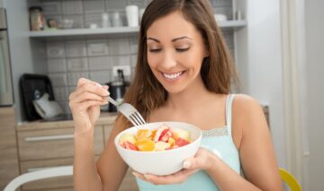 O femeie frumoasă care mănâncă fructe pe stomacul gol dintr-un bol alb