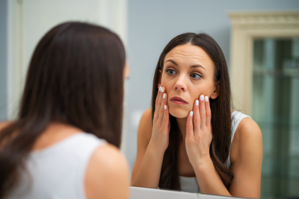 O femeie care s-a trezit cu fața umflată și se uită în oglindă