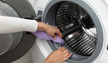 O femeie care curăță cu o lavetă mov mașina de spălat