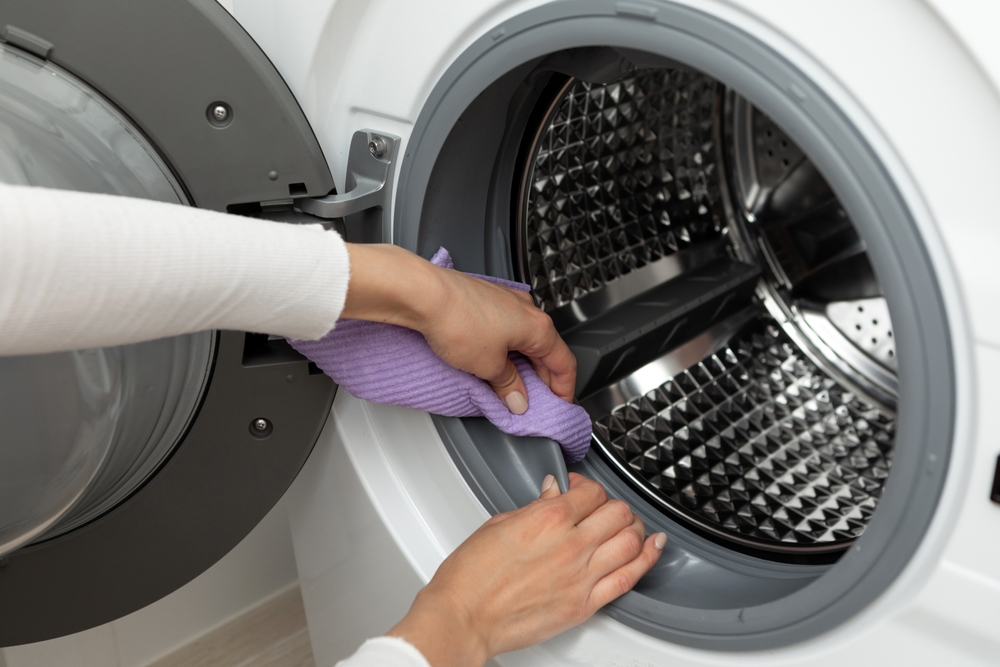 O femeie care curăță cu o lavetă mov mașina de spălat