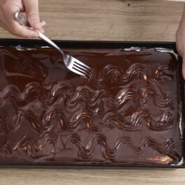 Femeie realizând dungi cu furculița peste glazura de ciocolată