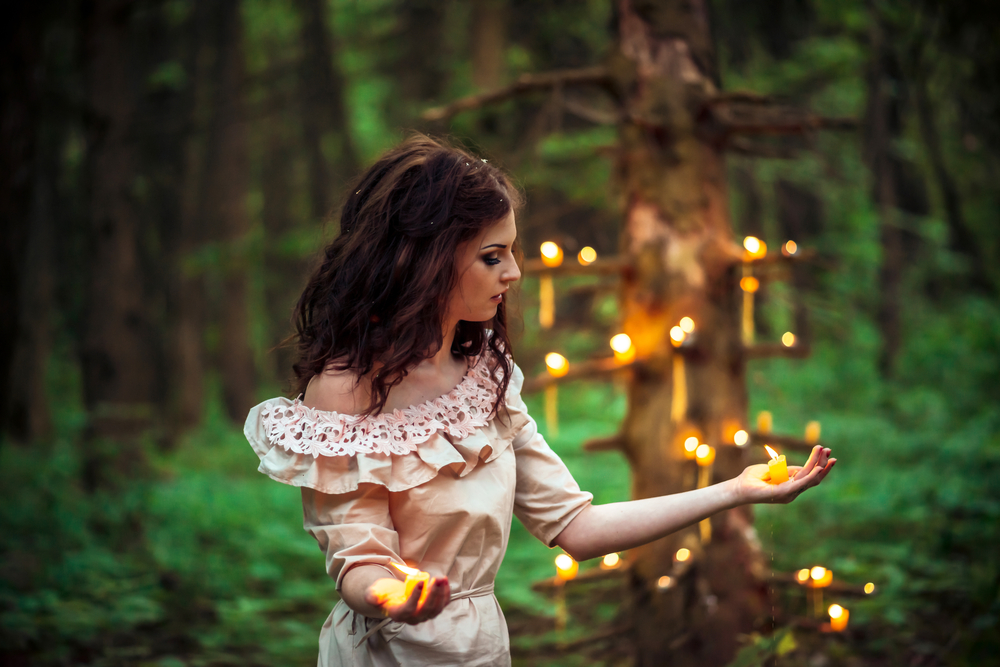 O femeie într-o pădure, cu multe lumânări aprinse în spate