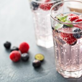 Două pahare, unul cu apă plată și unul cu apă minerală cu fructe pentru a ilustra cât de sănătoasă este apa plată în comparație cu apa minerală