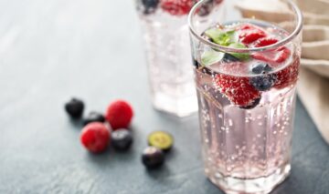 Două pahare, unul cu apă plată și unul cu apă minerală cu fructe pentru a ilustra cât de sănătoasă este apa plată în comparație cu apa minerală