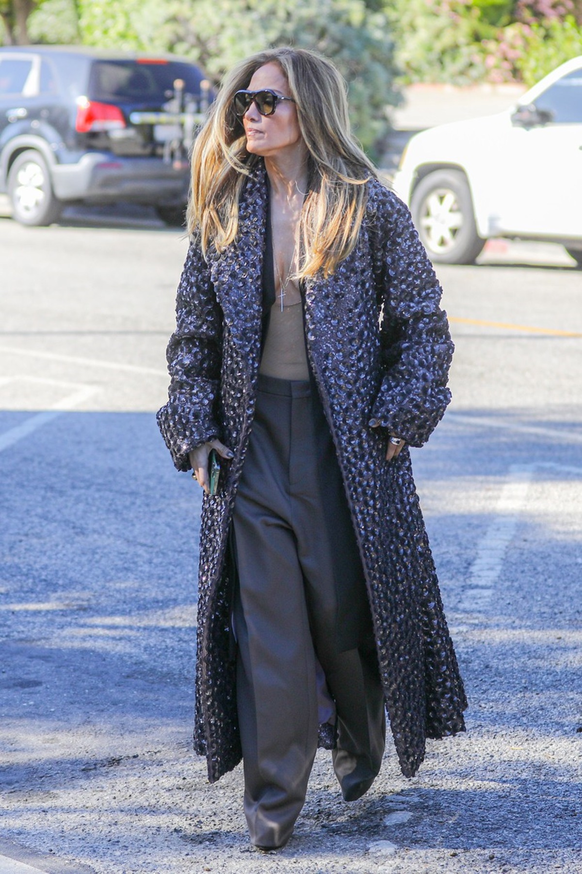 Jennifer Lopez cu o jachetă gri și o pereche de pantaloni largi în timp ce se plimbă pe stradă și își lasă la vedere decolteul adânc