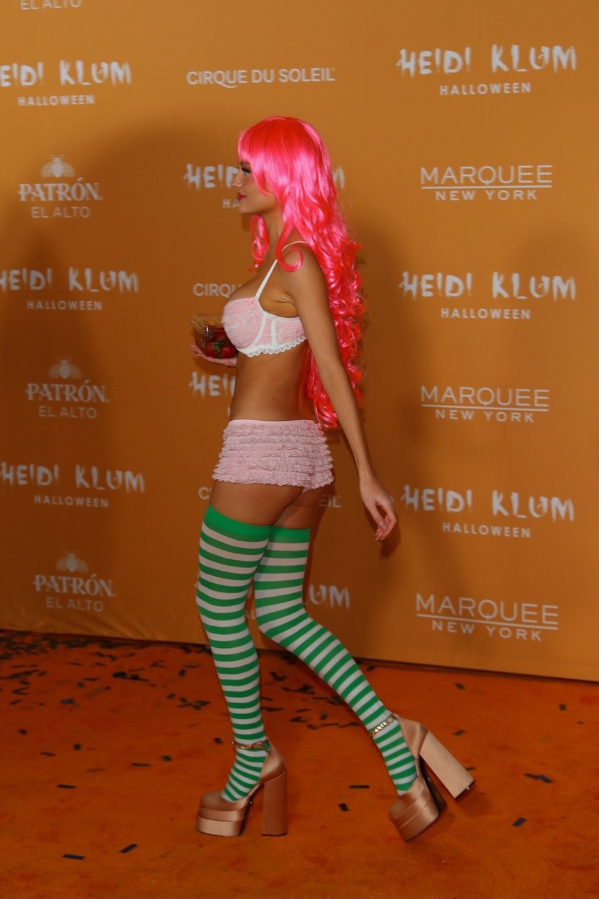 Leni Klum într-o pereche de șosete verzi, un sutien roz și pantaloni scurți în timp ce pozează ca personajul Căpșunica