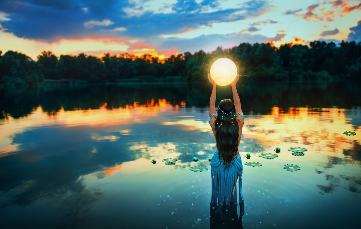 O femeie frumoasă care stă într-un lac și ține în mâini luna pentru a ilustra ce impact are Luna Plină în Gemeni pe data de 27 noiembrie 2023