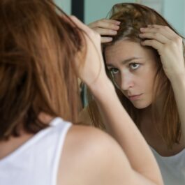 O femeie frumoasă care se privește în oglindă și încearcă să scape de scalpul uscat
