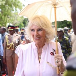 Regina Camilla care ține o umbreluță de soare și salută oamenii în timpul turneului din Africa