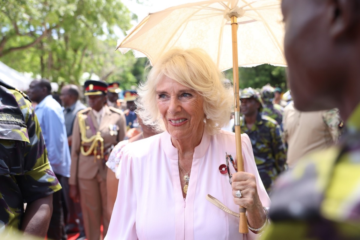 Regina Camilla care ține o umbreluță de soare și salută oamenii în timpul turneului din Africa