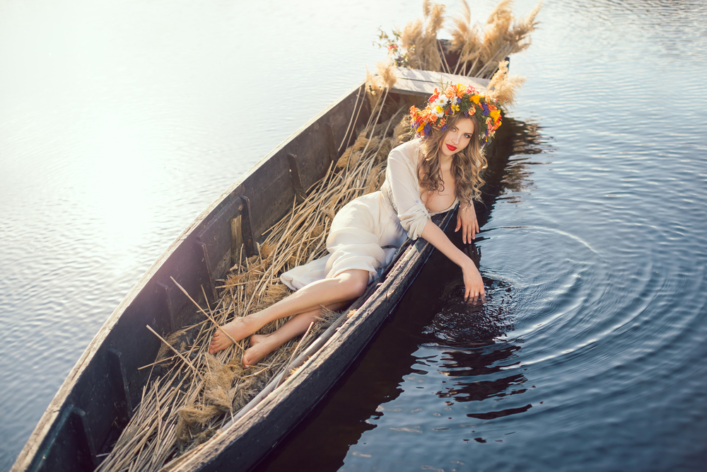 O femeie îmbrăcată într-o rochie albă, transparentă, într-o barcă care plutește pe lac