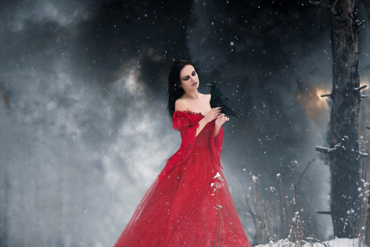 O femeie frumoasă care poartă o rochie roșie și stă într-o pădure în care a nins pentru a ilustra una dintre cele trei zodii care nu se feresc să-și ascundă invidia