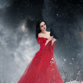 O femeie frumoasă care poartă o rochie roșie și stă într-o pădure în care a nins pentru a ilustra una dintre cele trei zodii care nu se feresc să-și ascundă invidia