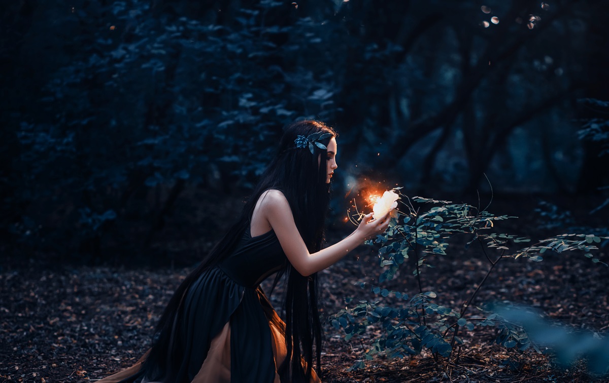O femeie frumoasă care poartă o rochie neagră și privește o plantă luminată, ea simbolizând una dintre cele trei zodii care pierd bani în luna noimebrie 2023