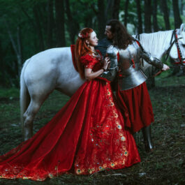 O femeie în rochie roșie, alături de un cavaler, într-o pădure