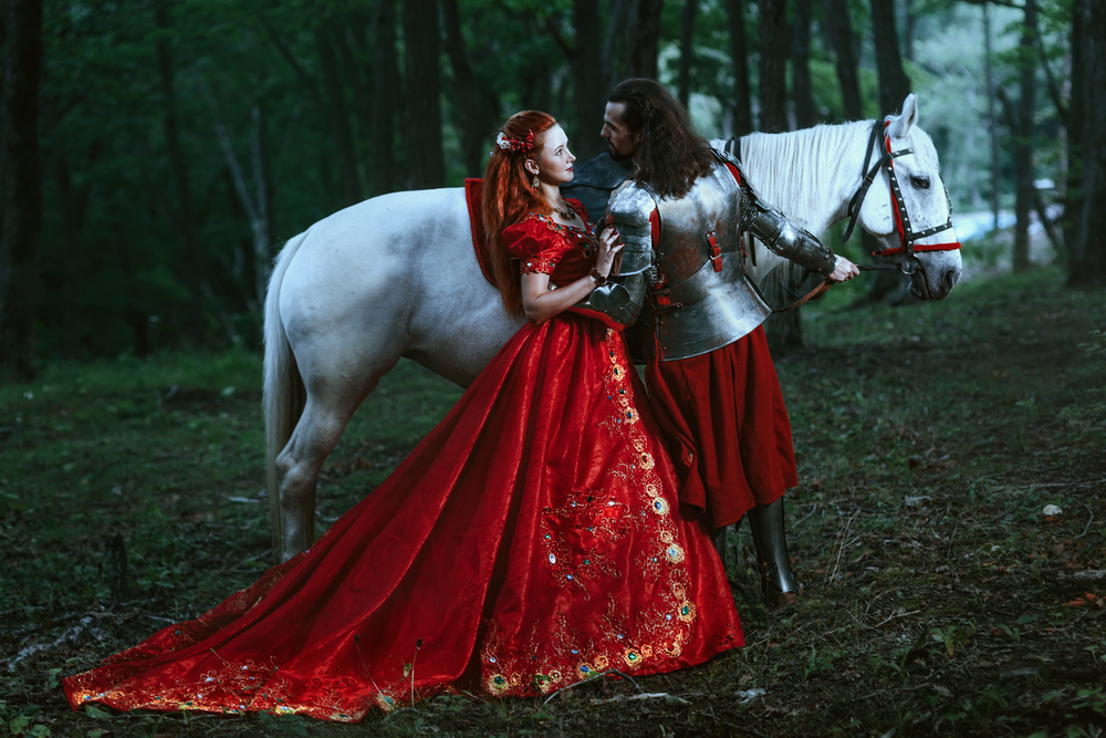O femeie în rochie roșie, alături de un cavaler, într-o pădure