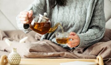 O femeie într-un pulover gri, care pune ceai într-o ceașcă