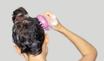 O femeie care își spală părul și folosește o perie de masaj pentru scalp