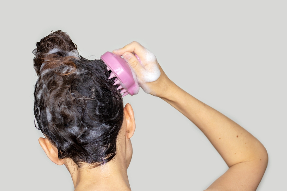 O femeie care își spală părul și folosește o perie de masaj pentru scalp