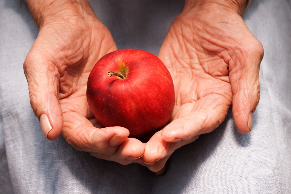 O femeie în vârstă care ține un măr în palme