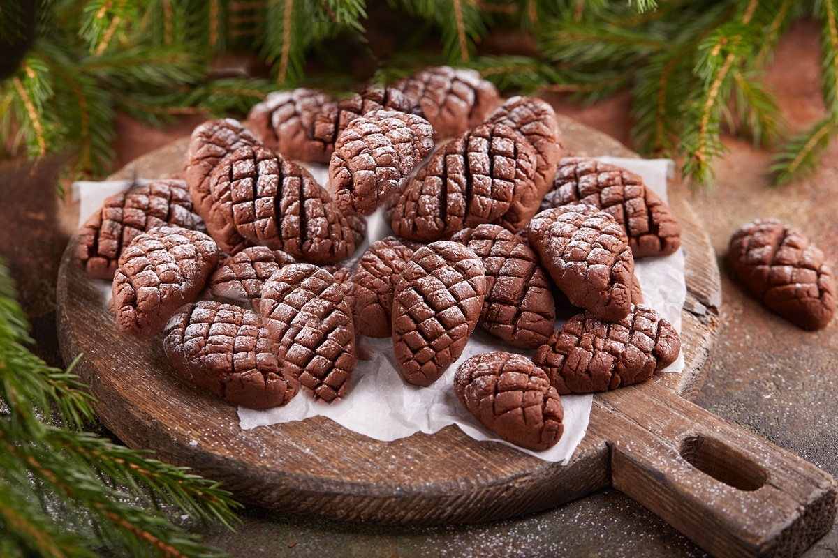 Biscuiți conuri de brad, cu cacao și aromă de rom pe un tocător de lemn rotund, înconjurat de crengi de brad