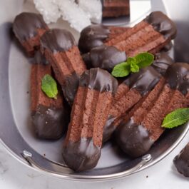 Biscuiți șprițați cu ciocolată pe un platou, decorați cu frunze de mentă