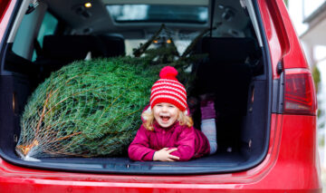 O fetiță care stă în portbagajul mașinii alături de bradul de Crăciun
